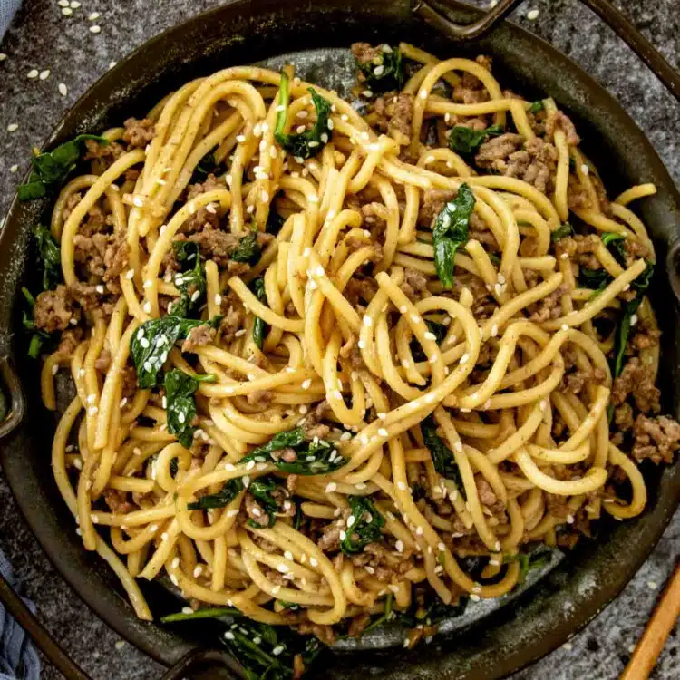 a serving of pork noodle stir fry in a brown metal plate.