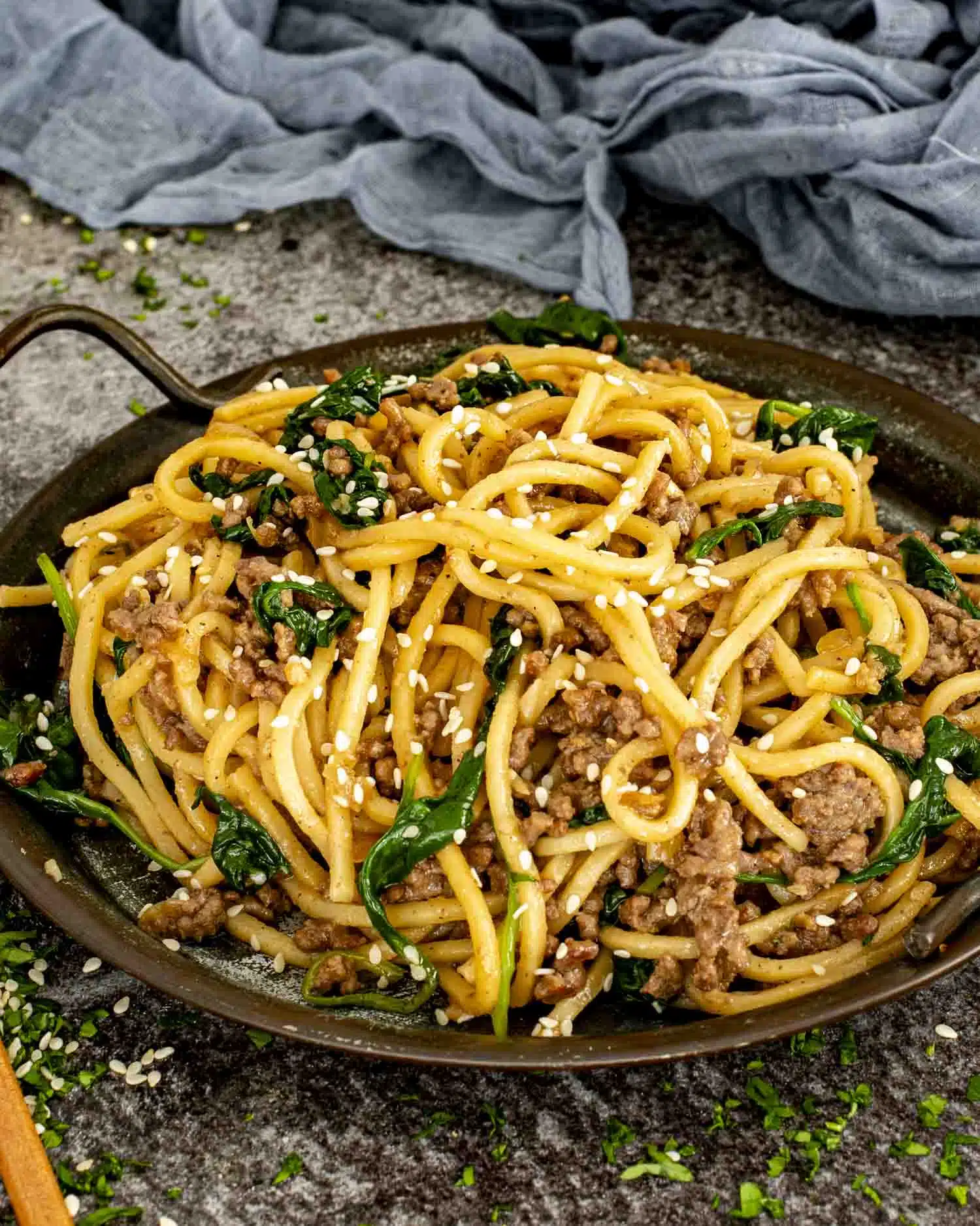 a serving of pork noodle stir fry in a brown metal plate.