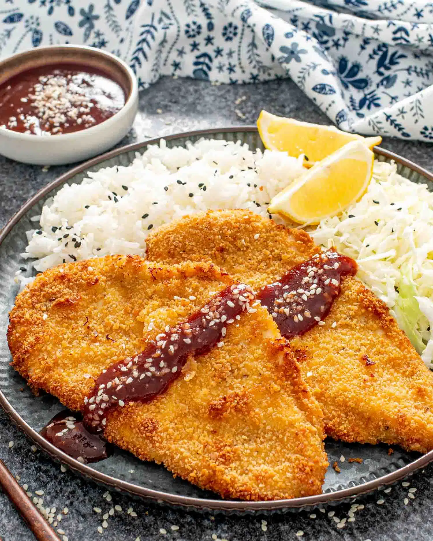 2 pieces of chicken katsu with tonkatsu sauce with rice and 2 lime wedges.