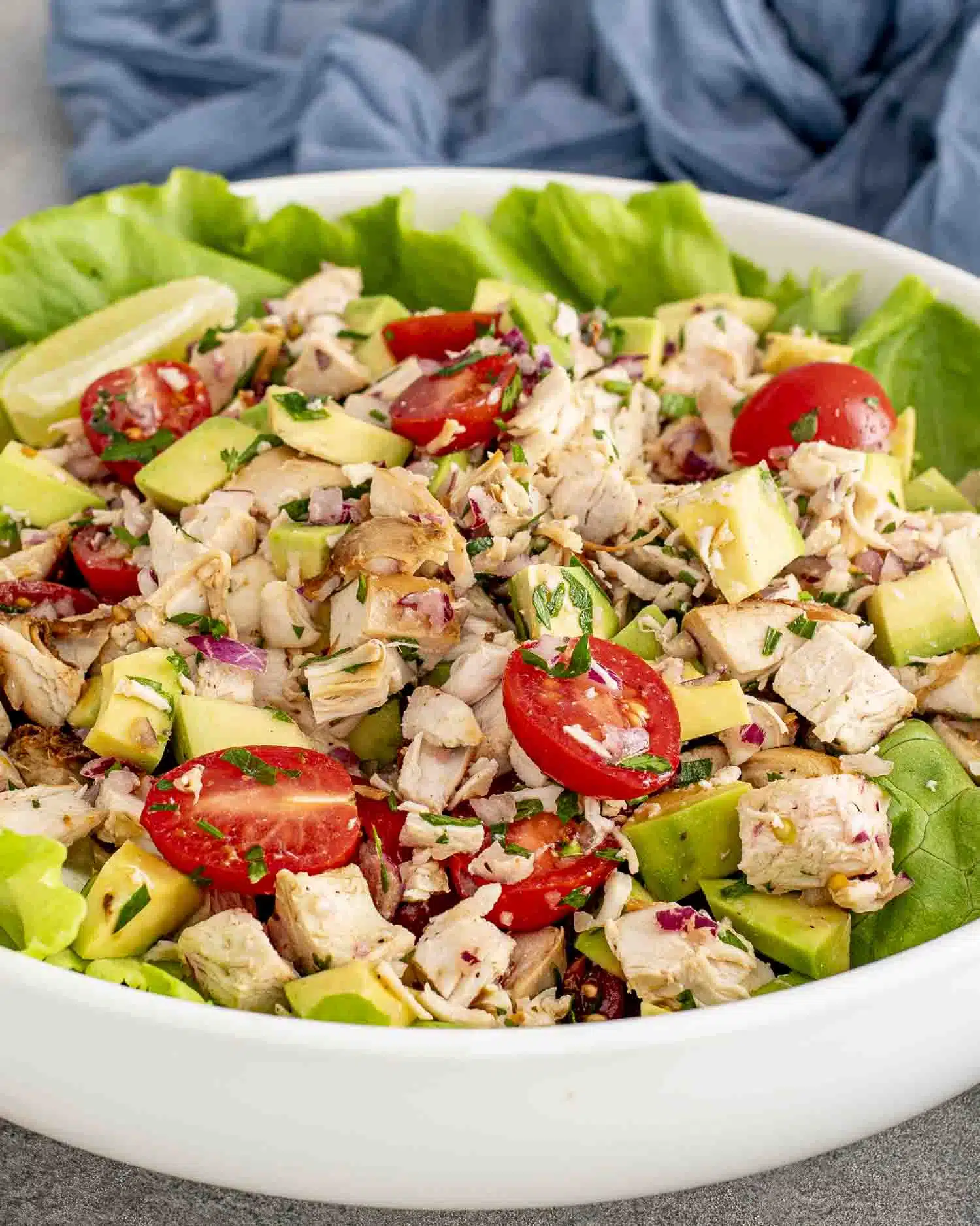freshly made avocado chicken salad in a large white bowl on top of a bed of lettuce.