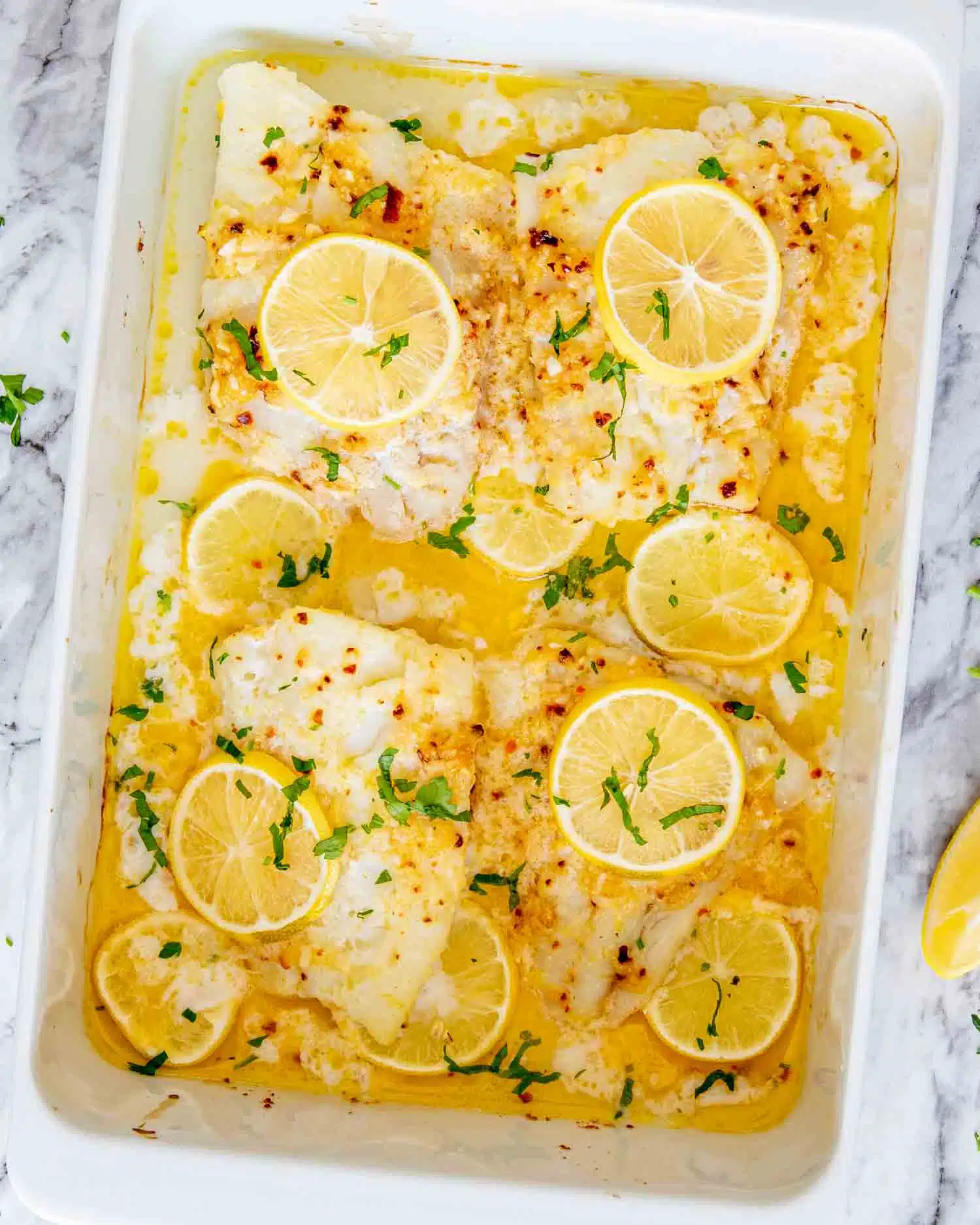 freshly baked lemon butter cod in a white baking pan.