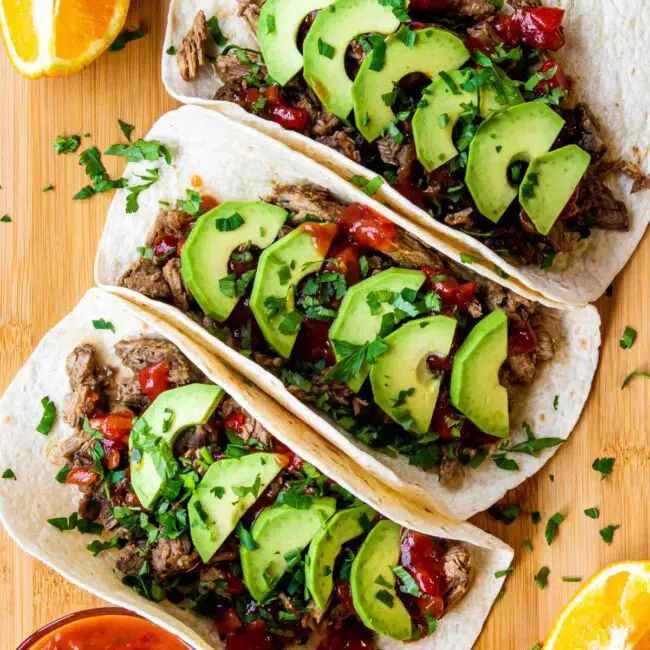 3 beef carnitas tacos on a cutting board.