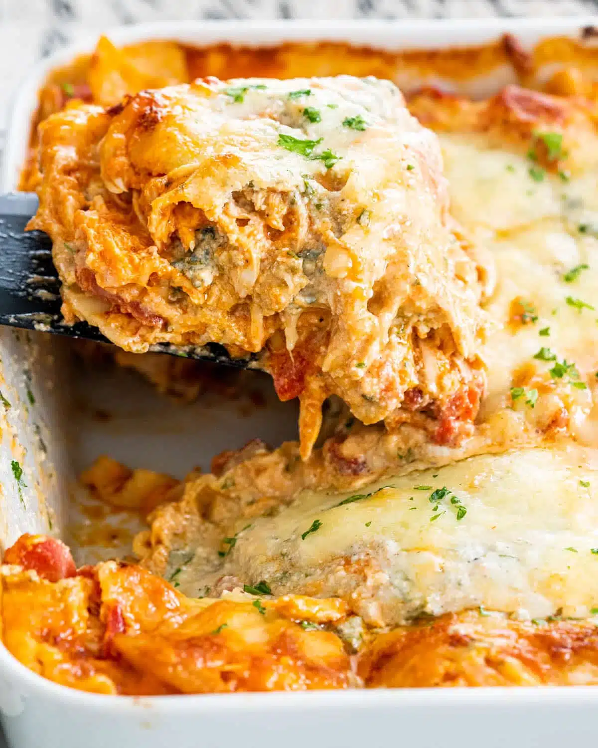 a spatula pulling a slice of lasagna from a casserole dish