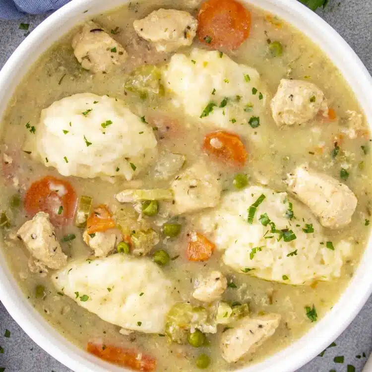 Bowl of chicken and dumplings with tender chicken, vegetables, and fluffy dumplings in a creamy broth, garnished with parsley.
