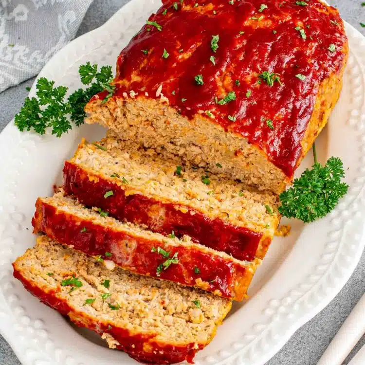 sliced up chicken meatloaf on a white serving platter garnished with parsley.