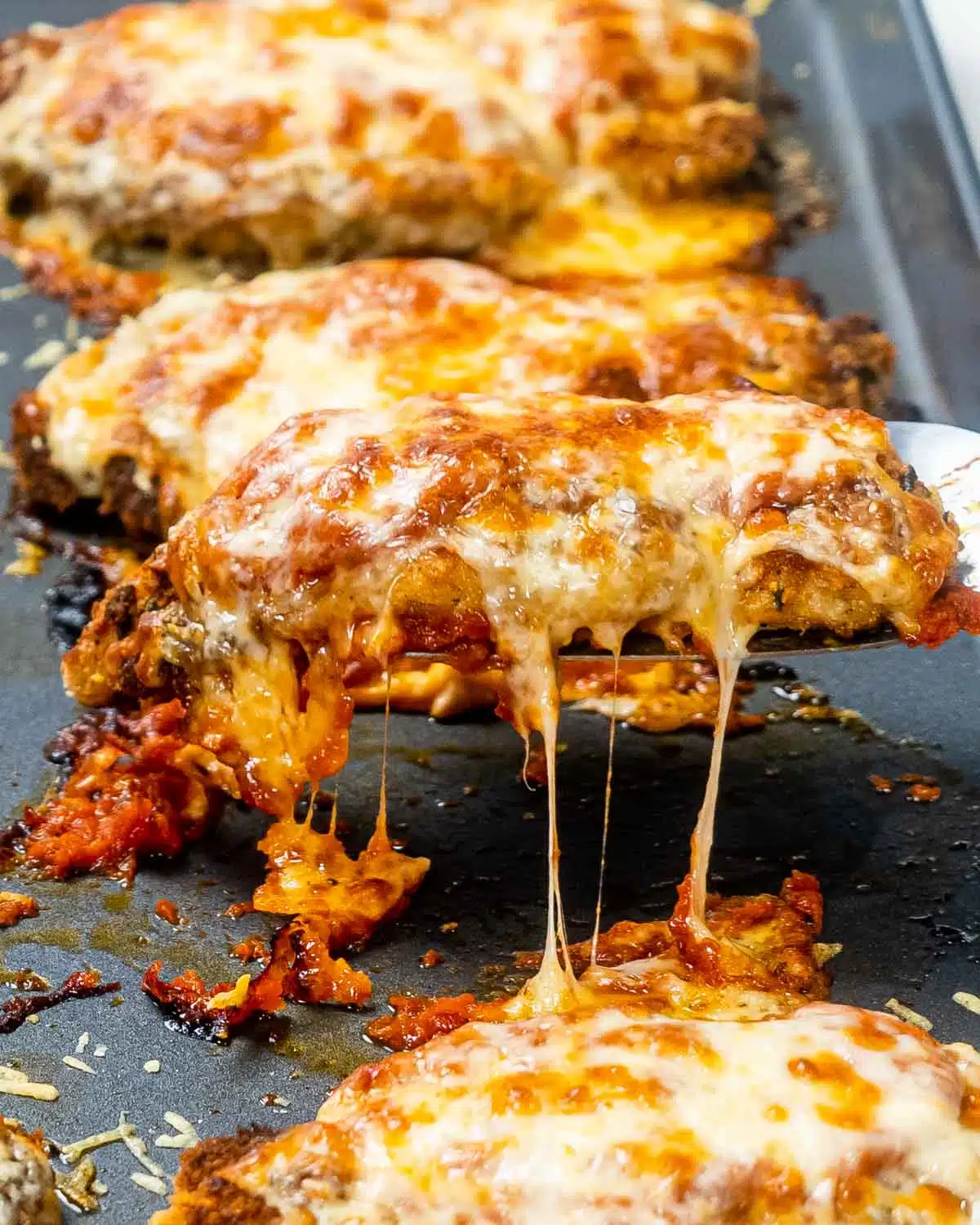 a spatula lifting a piece of chicken parmesan from a baking sheet.