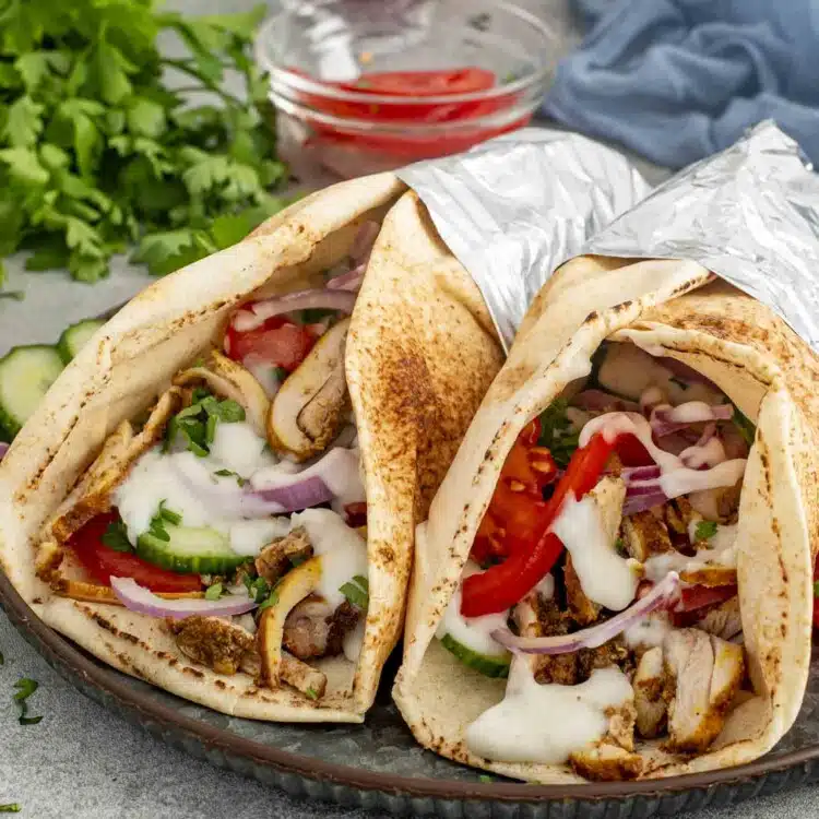 Two Chicken Shawarma wraps in pita bread, filled with juicy chicken, tomatoes, red onions, and drizzled with tzatziki sauce.