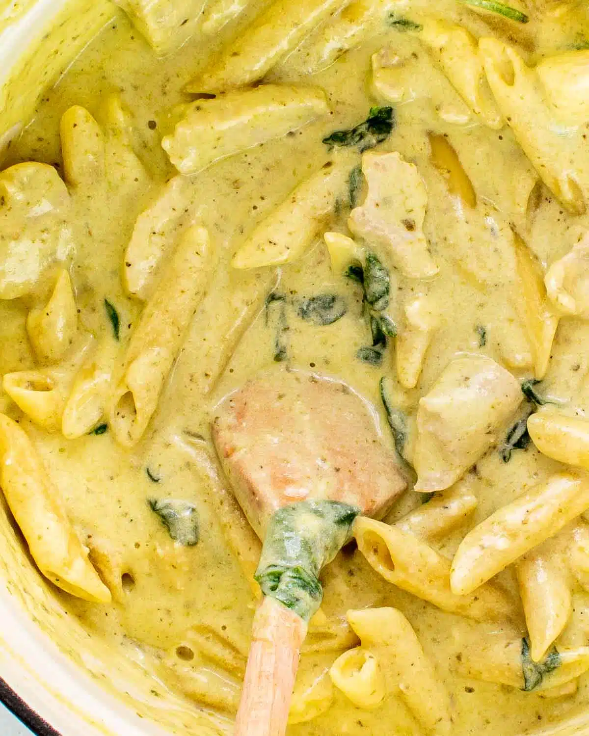 freshly made creamy pesto chicken pasta in a dutch oven with a wooden spoon inside.