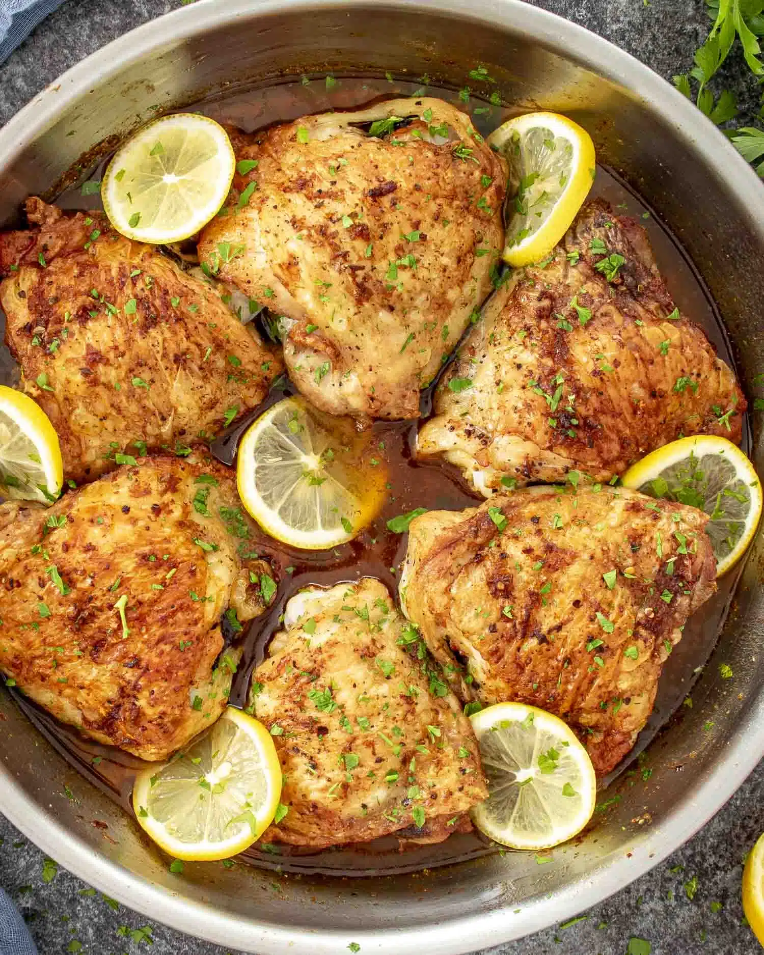 crispy lemon chicken thighs fresh out of the oven in a skillet garnished with parsley and lemon slices.
