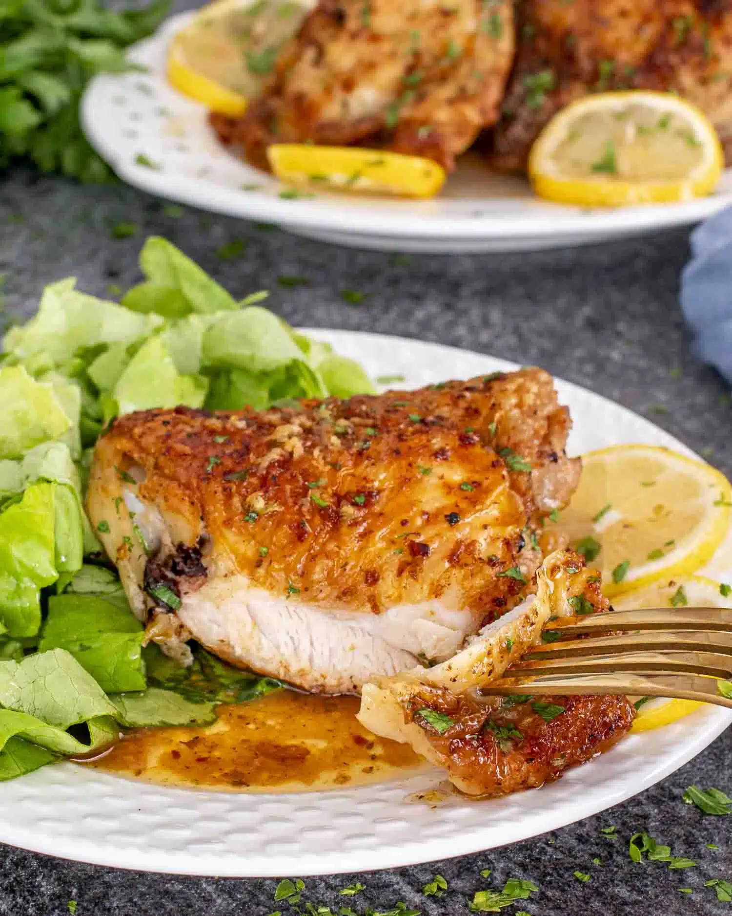a crispy lemon chicken thigh on a white plate with a lettuce salad on the side.