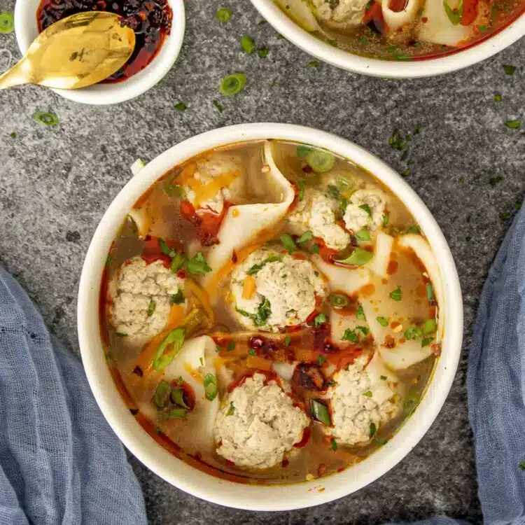 a beige bowl loaded with deconstructed wonton soup and garnished with chili oil.