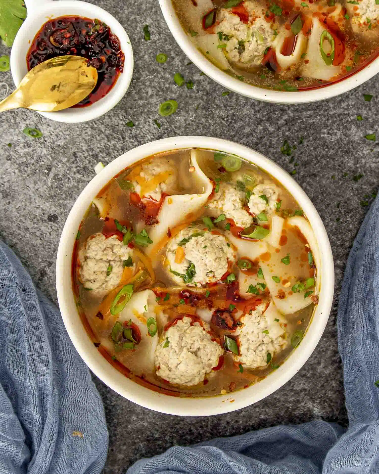 a beige bowl loaded with deconstructed wonton soup and garnished with chili oil.