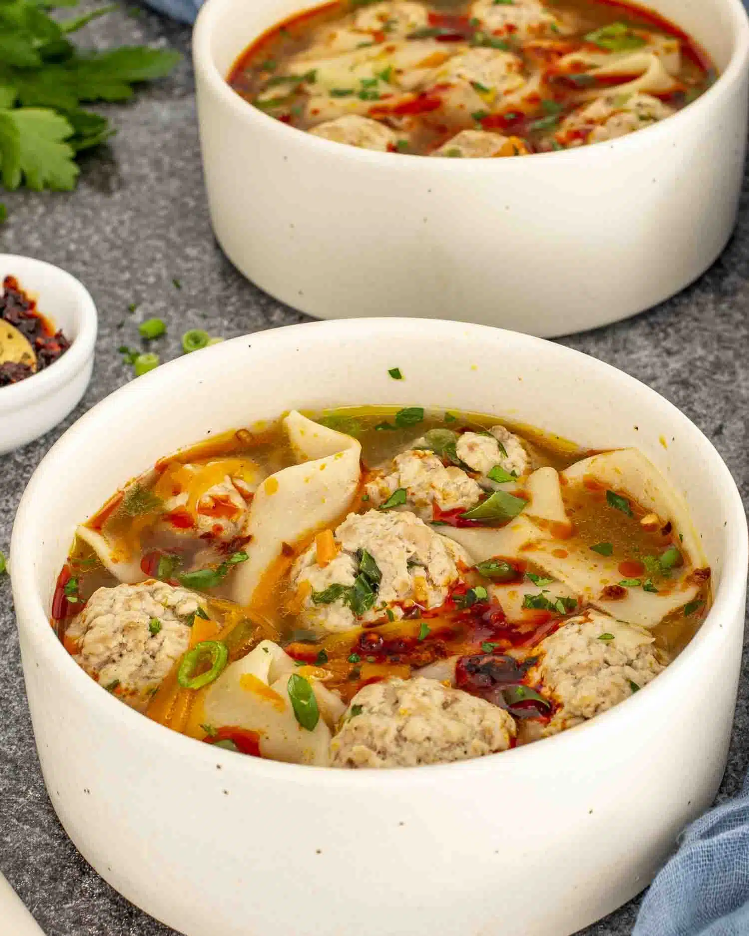 a beige bowl loaded with deconstructed wonton soup and garnished with chili oil.