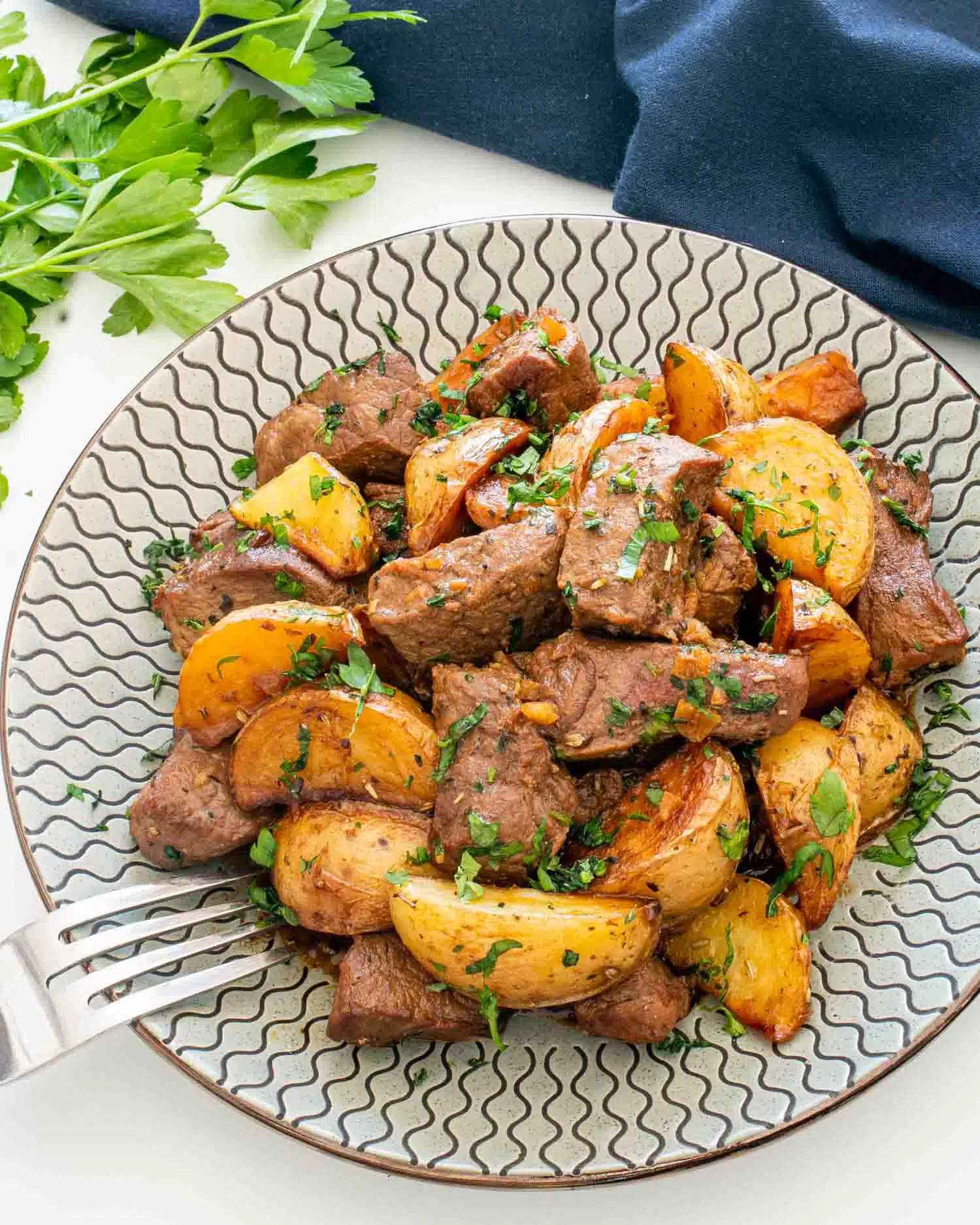 garlic butter steak and potatoes serving on a plate garnished with parsley.