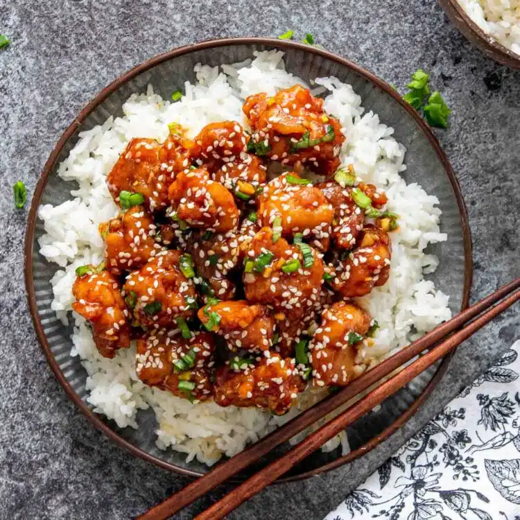 general tso's chicken over a bed of rice in a plate with chop sticks.