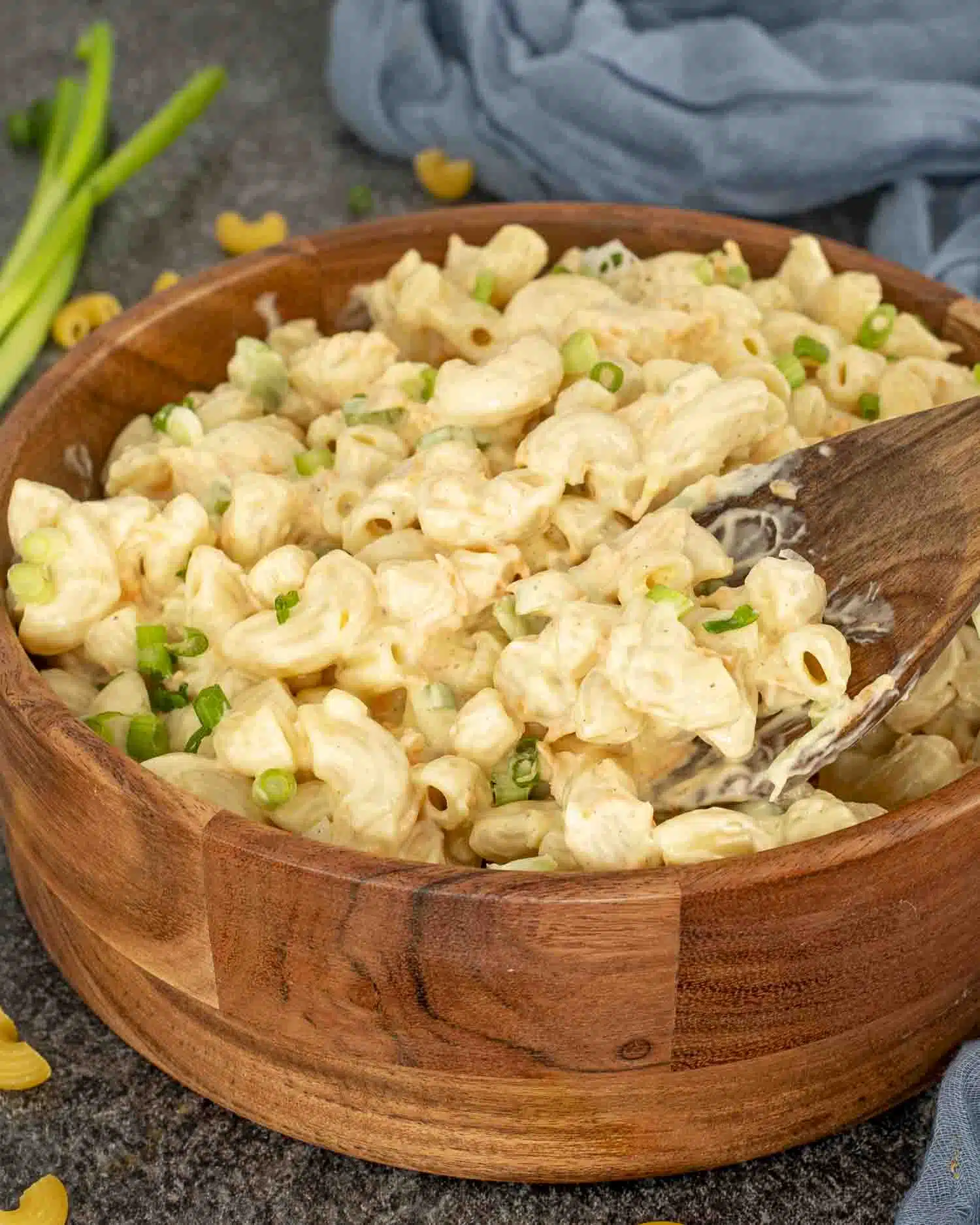 Creamy Hawaiian macaroni salad in a wooden bowl garnished with sliced green onions, set on a gray textured surface.