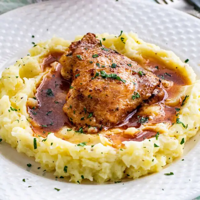 chicken thigh with gravy on a bed of mashed potatoes.