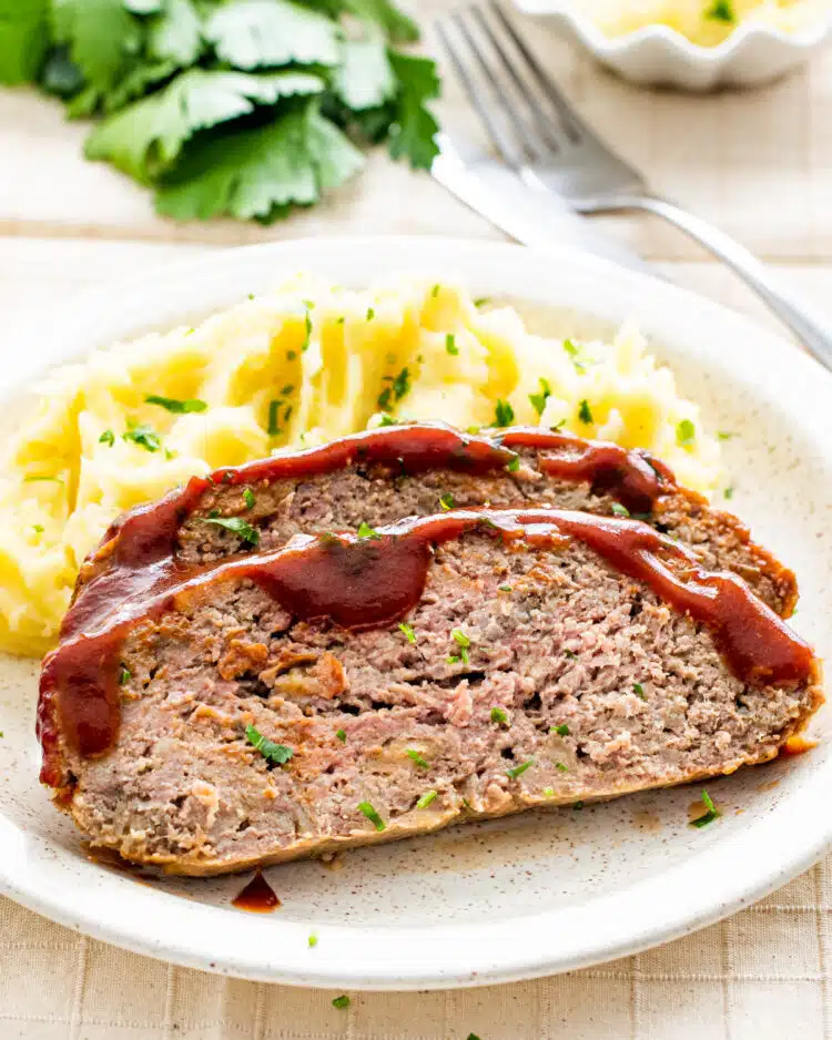2 slices of meatloaf next to mashed potatoes on a plate