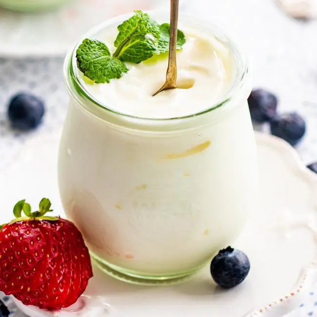 yogurt in a serving jar with a spoon standing garnished with mint and berries.
