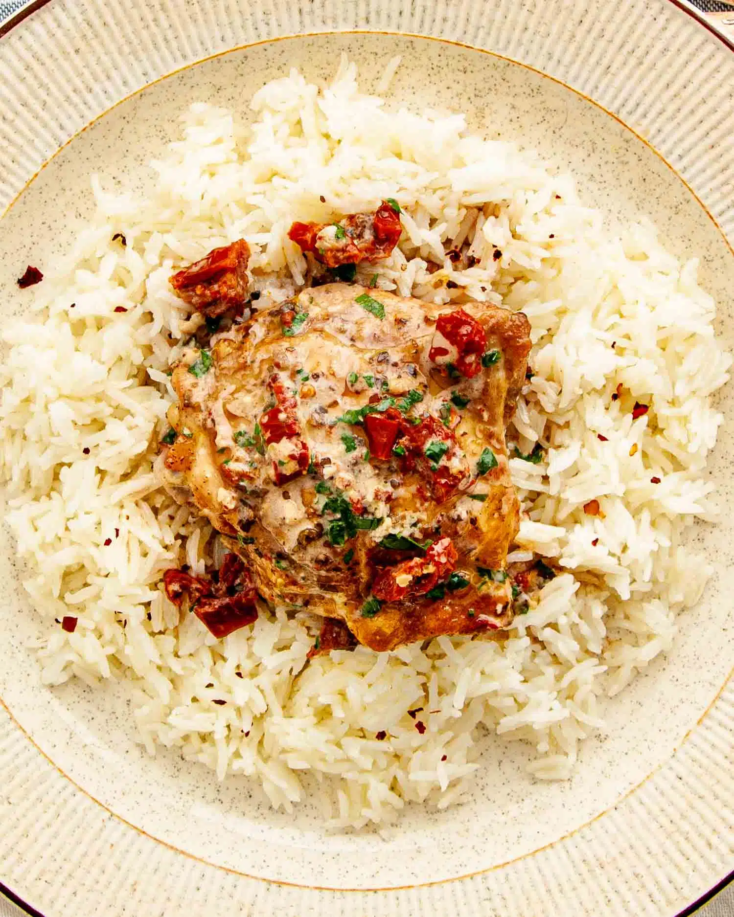 a serving of marry me chicken on a bed of rice in a beige dinner plate.