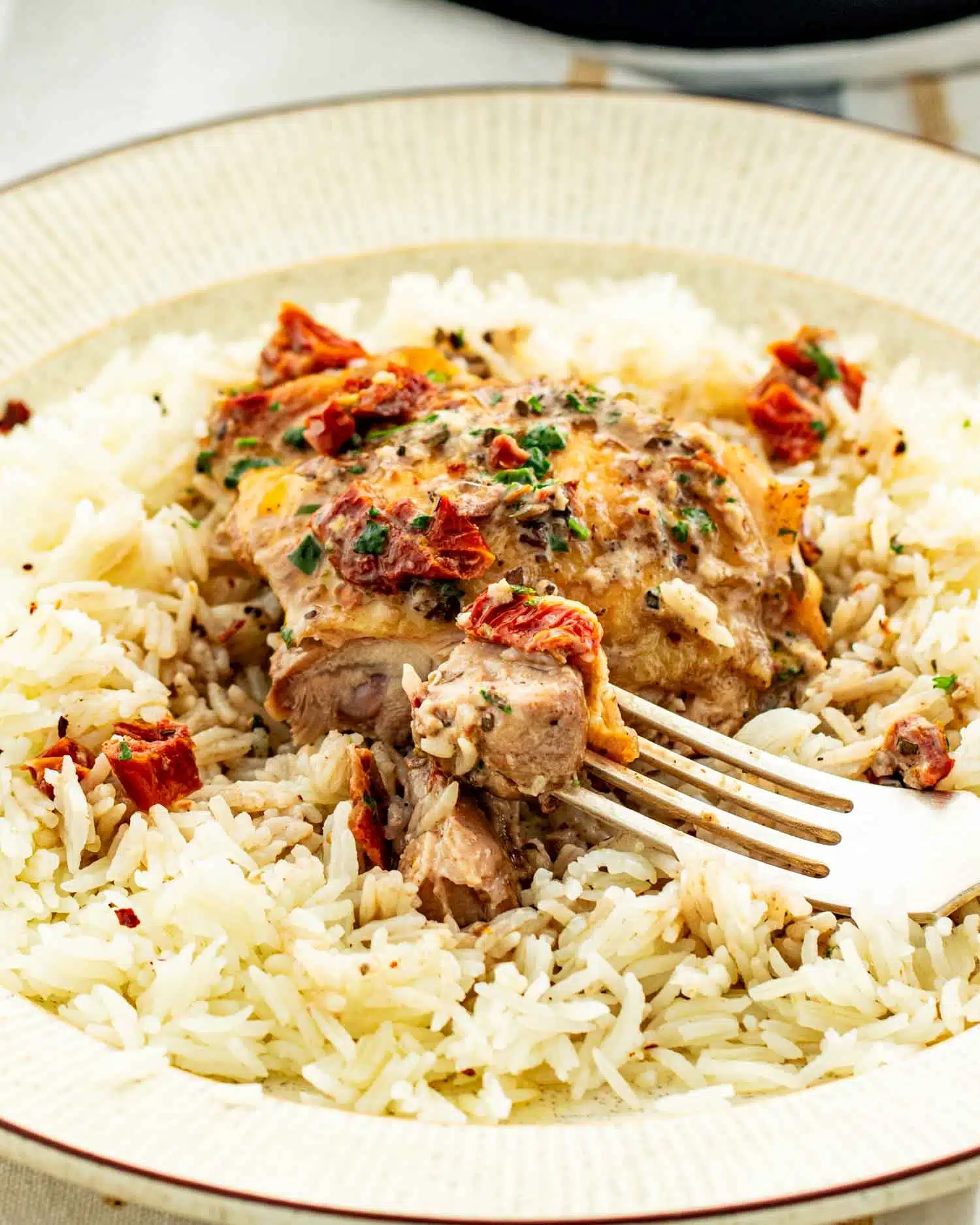 a serving of marry me chicken on a bed of rice in a beige dinner plate.