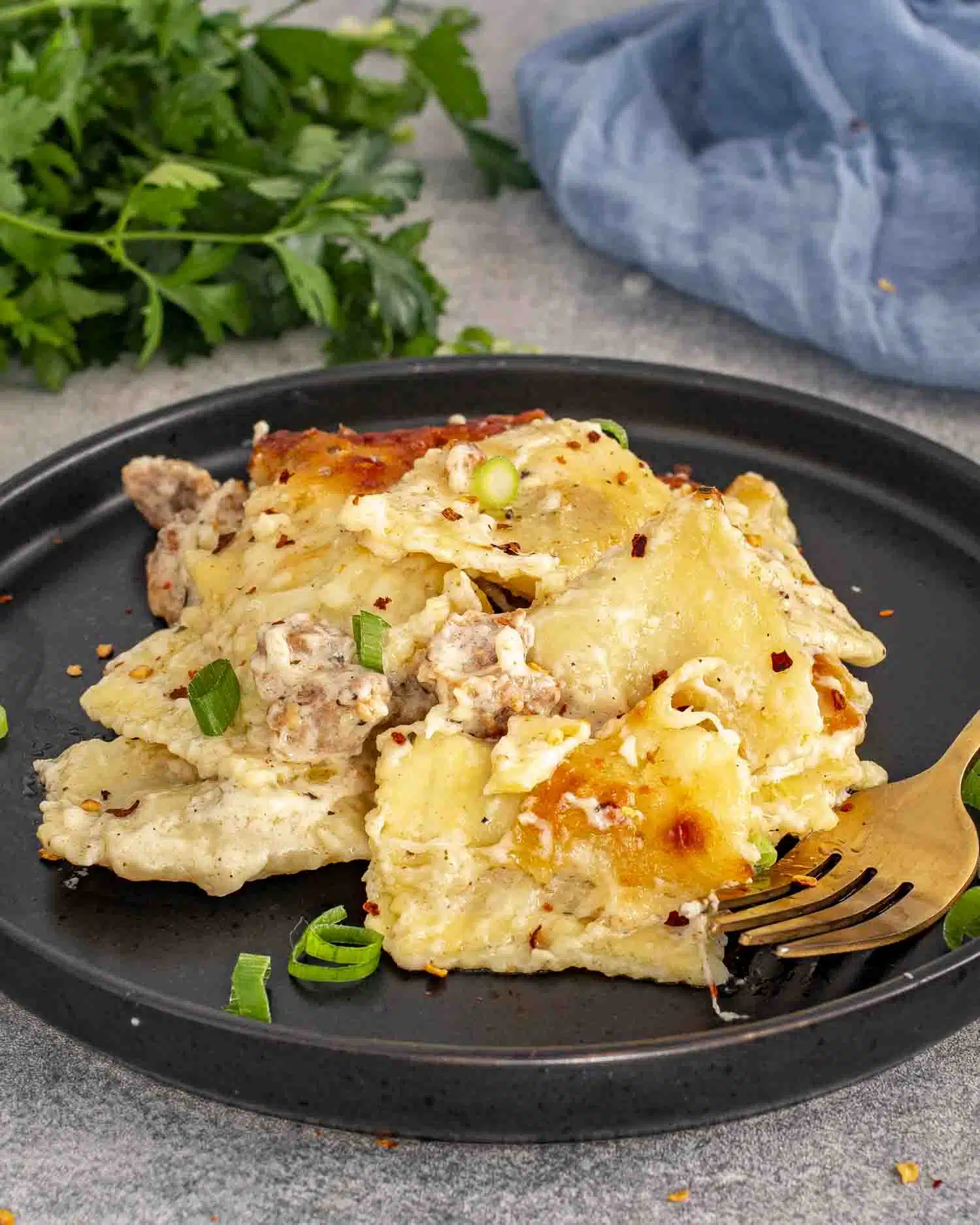 a serving of ravioli alfredo bake on a black plate.