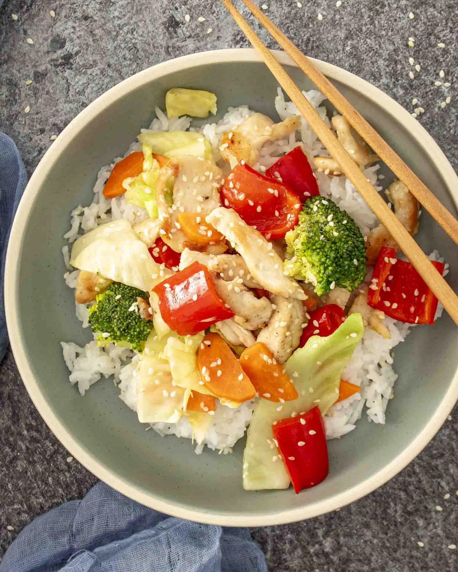 a serving of stir fried chicken and veggies in white sauce over a bed of rice in a bowl.