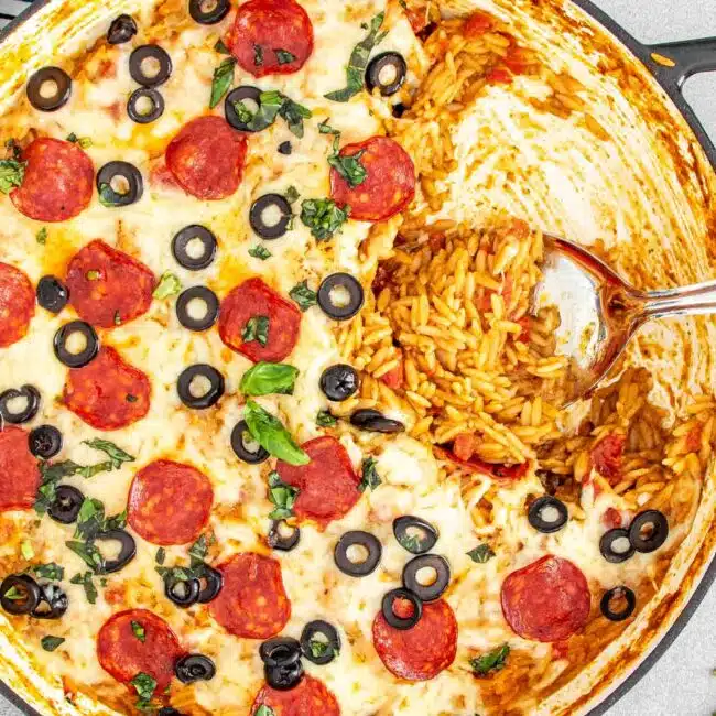 Golden-bubbly Skillet Pizza Pesto Orzo topped with pepperoni, olives, and fresh basil in a cast iron pan.