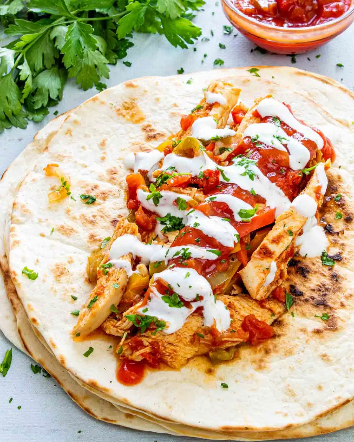 chicken fajitas on a tortilla garnished with sour cream and limes.