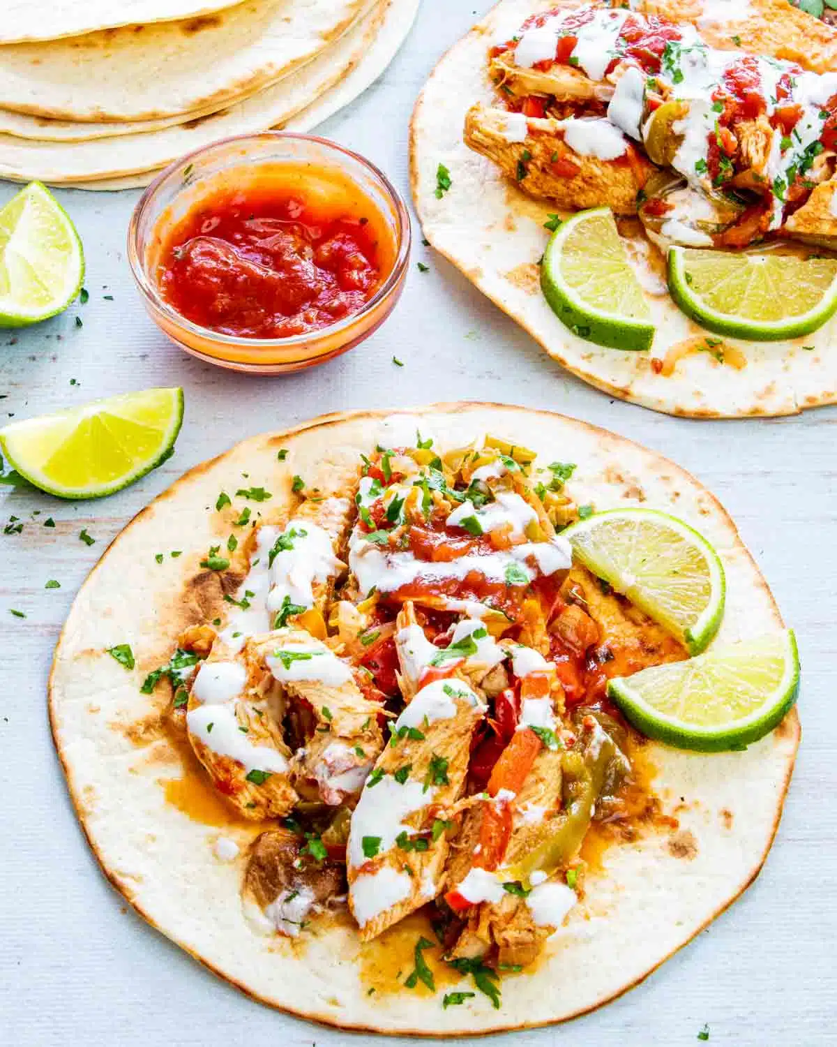 chicken fajitas on a tortilla garnished with sour cream and limes.