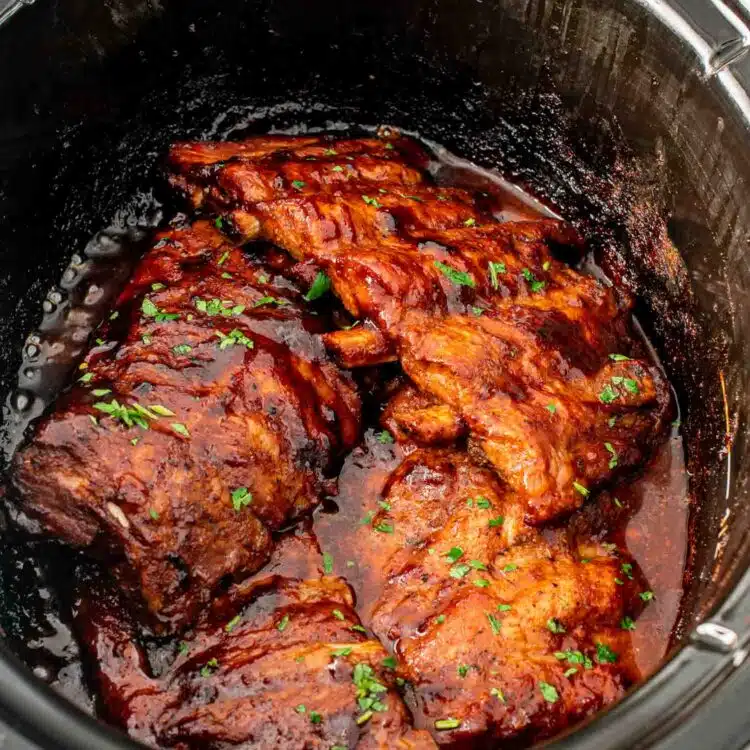 freshly made slow cooker ribs right in the slow cooker with bbq sauce and garnished with parsley.