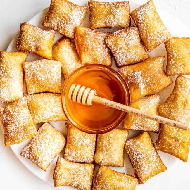 sopapillas on a big white plate with a bowl with honey in the middle.