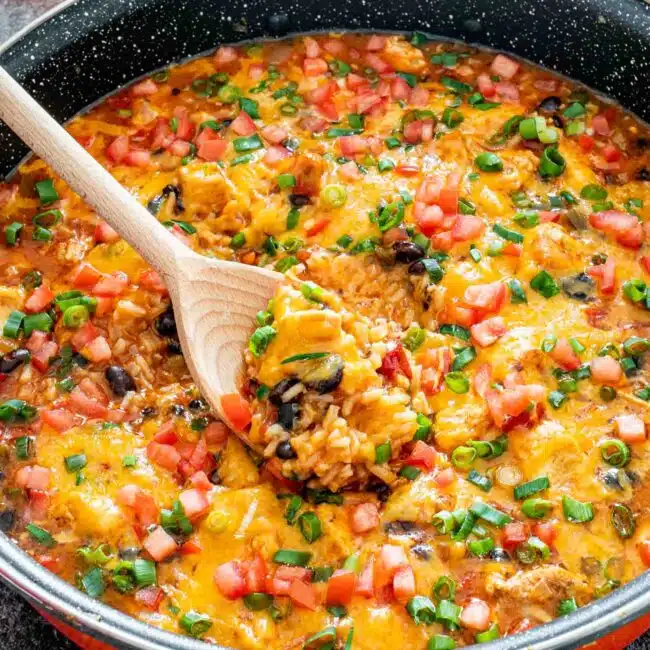 southwest chicken and rice in a skillet with a wooden spoon inside.