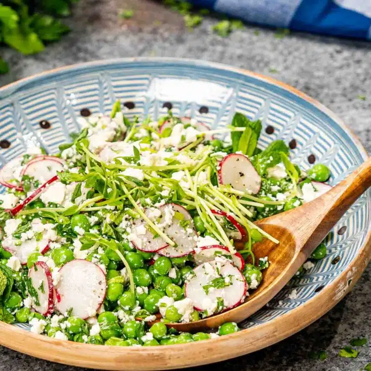 spring pea salad on a clay plate with a wooden spoon.